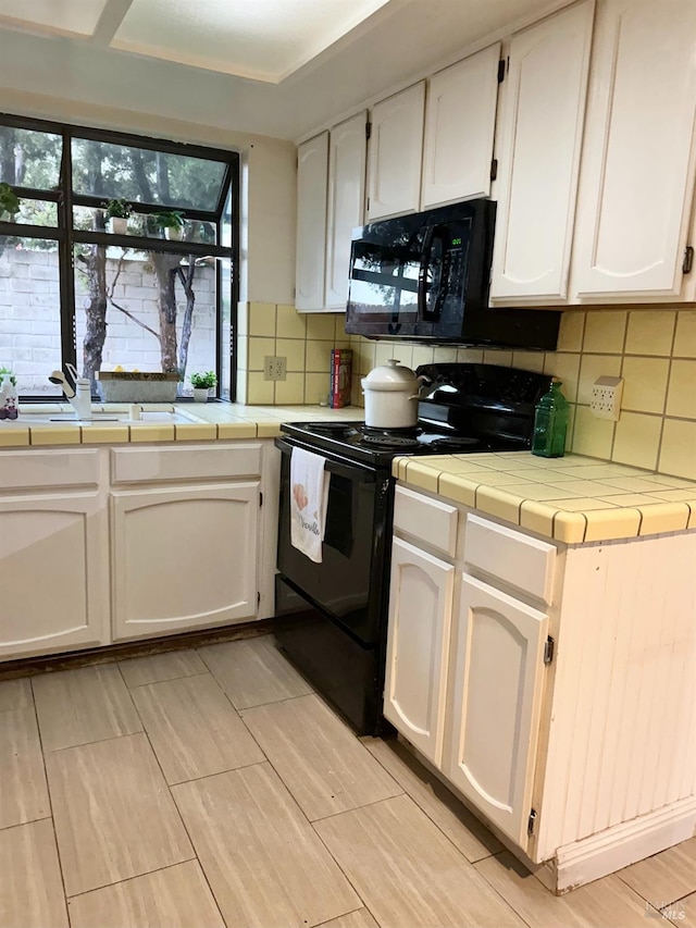 kitchen featuring white cabinets, black appliances, tile countertops, and backsplash