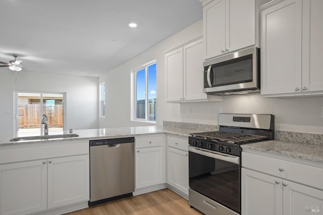 kitchen with light wood-type flooring, stainless steel appliances, ceiling fan, sink, and white cabinets