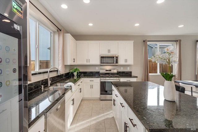 kitchen featuring white cabinetry, sink, dark stone counters, light tile patterned floors, and appliances with stainless steel finishes