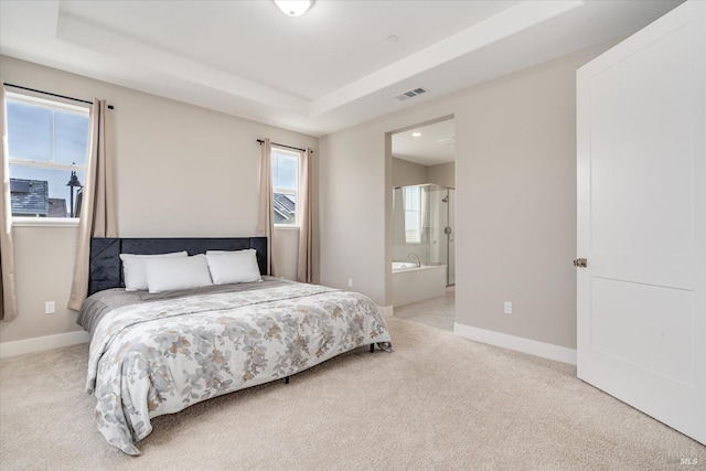 bedroom with light carpet, a raised ceiling, and ensuite bath