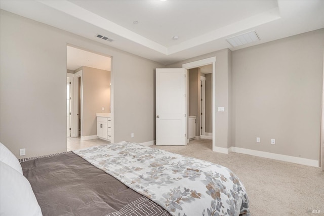 carpeted bedroom with a raised ceiling and connected bathroom