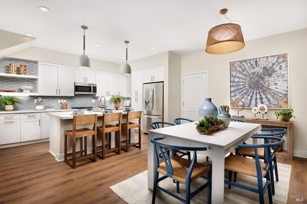 kitchen with white cabinets, pendant lighting, stainless steel appliances, and a kitchen island with sink