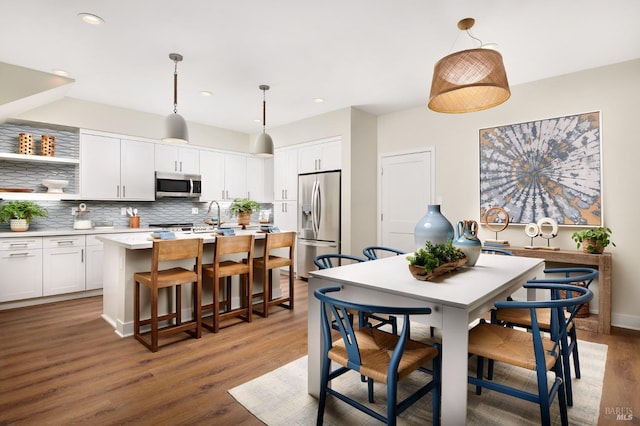 kitchen with white cabinets, pendant lighting, stainless steel appliances, and a kitchen island with sink