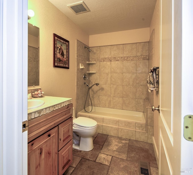 full bathroom with vanity, tiled shower / bath, toilet, and a textured ceiling