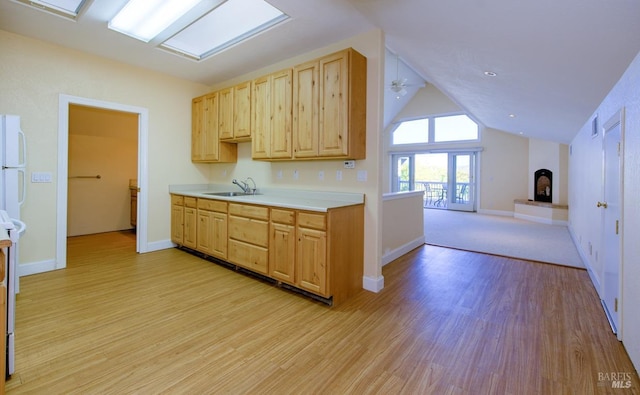 kitchen featuring sink, vaulted ceiling with skylight, light wood-type flooring, and light brown cabinets