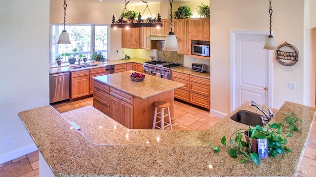 kitchen featuring appliances with stainless steel finishes, decorative light fixtures, sink, a kitchen bar, and a center island