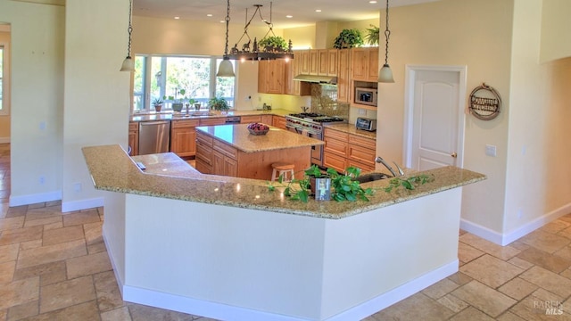 kitchen with light stone counters, appliances with stainless steel finishes, a kitchen island, pendant lighting, and backsplash