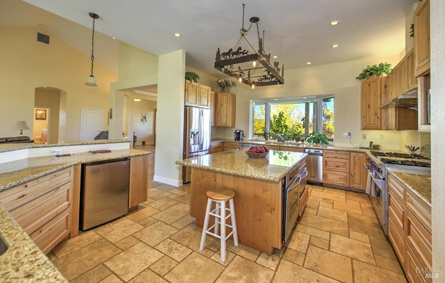 kitchen with appliances with stainless steel finishes, a kitchen bar, hanging light fixtures, a center island, and light stone counters