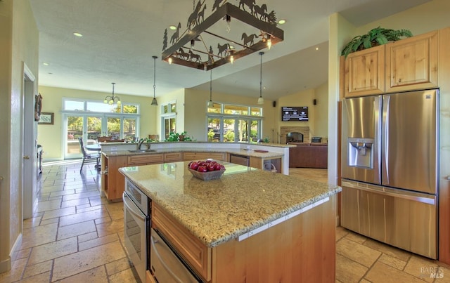 kitchen with hanging light fixtures, appliances with stainless steel finishes, kitchen peninsula, a kitchen island, and light stone countertops