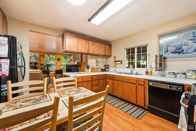 kitchen featuring brown cabinetry, black appliances, light wood finished floors, and a sink