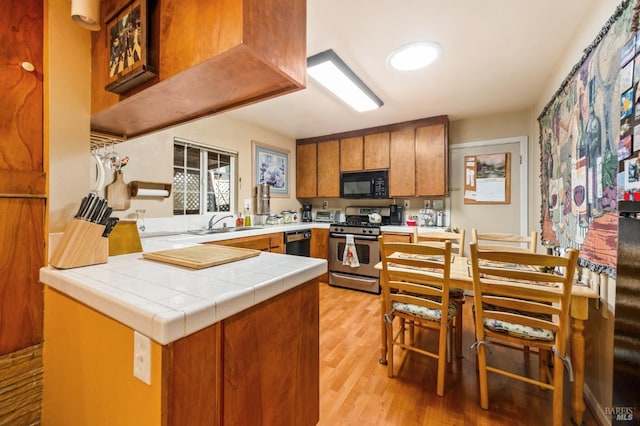 kitchen featuring a sink, a peninsula, brown cabinetry, black appliances, and light wood-style floors