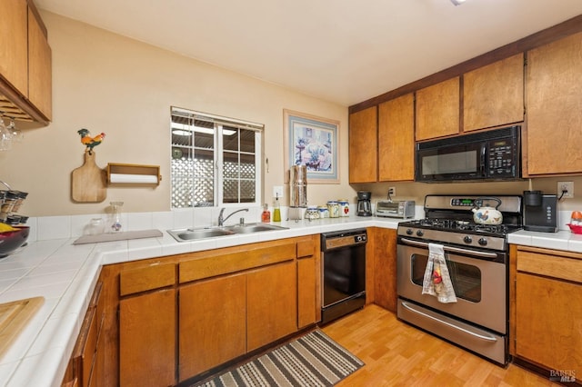 kitchen with a toaster, brown cabinetry, a sink, black appliances, and light wood-type flooring