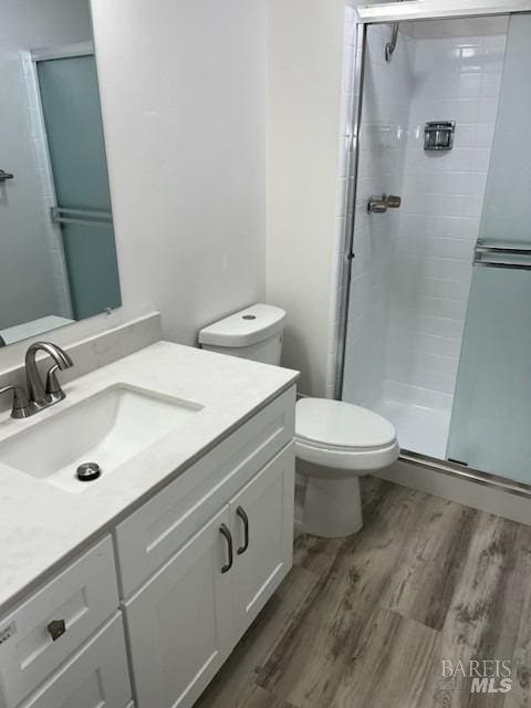 bathroom with vanity, wood finished floors, toilet, and a stall shower