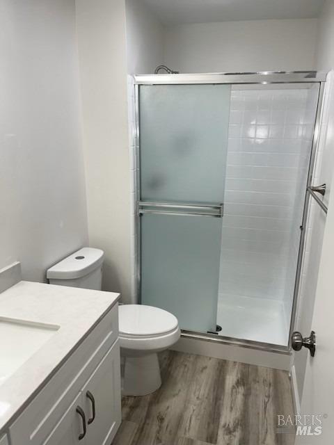 full bath featuring toilet, wood finished floors, a shower stall, and vanity