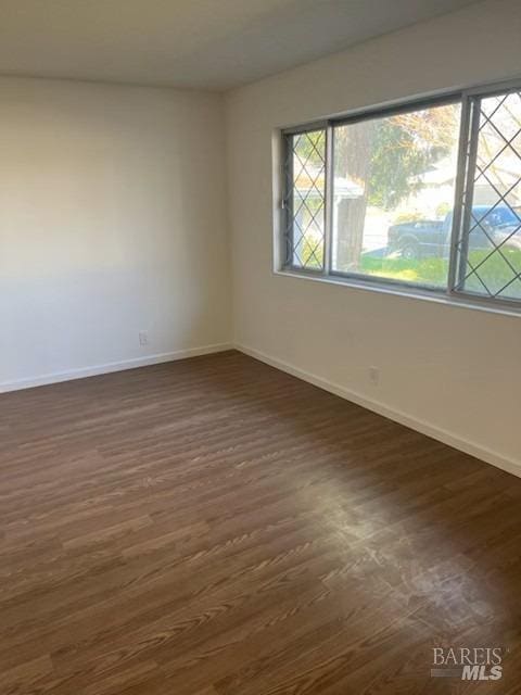 spare room featuring baseboards and dark wood finished floors