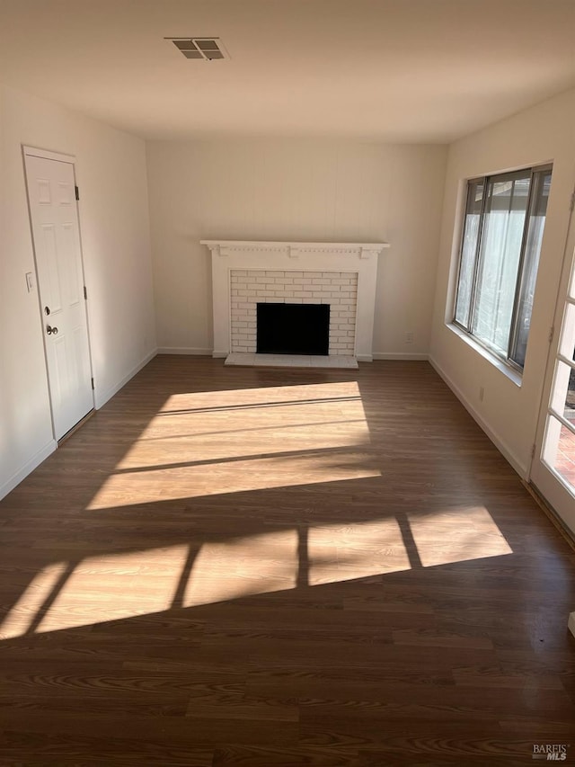 unfurnished living room with a fireplace, wood finished floors, visible vents, and baseboards