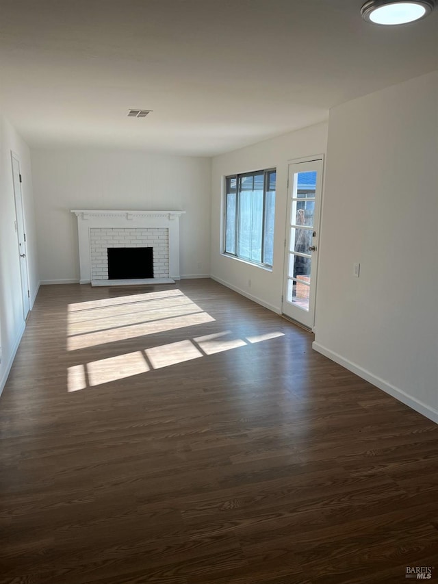 unfurnished living room featuring a fireplace, visible vents, dark wood finished floors, and baseboards
