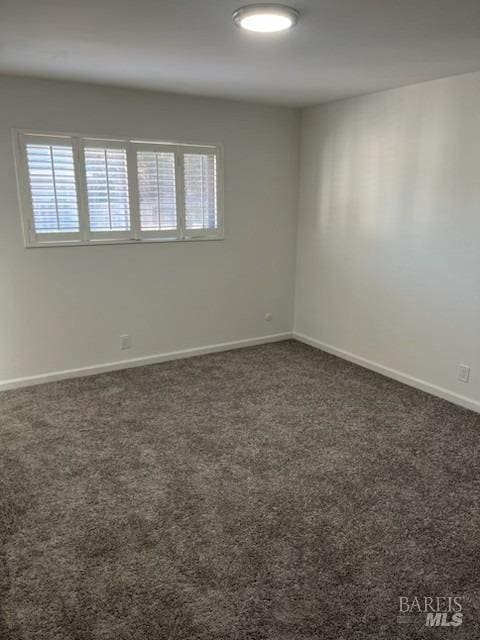 spare room featuring dark colored carpet and baseboards