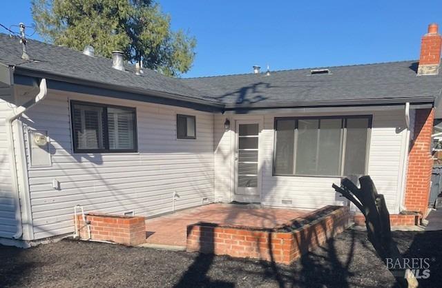 back of property featuring a chimney, a shingled roof, and a patio