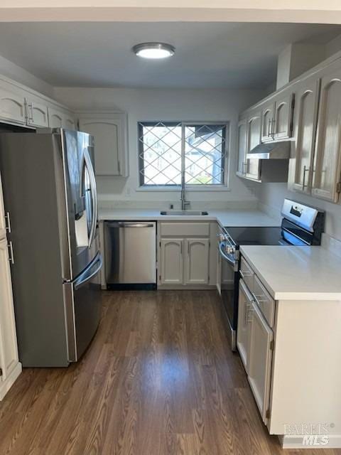 kitchen featuring a sink, stainless steel appliances, under cabinet range hood, light countertops, and dark wood finished floors