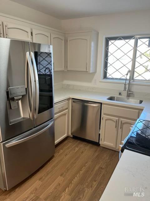 kitchen with stainless steel appliances, wood finished floors, light countertops, and a sink