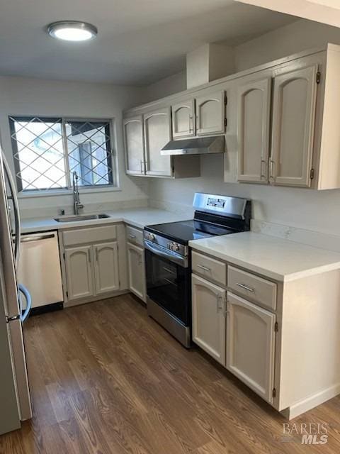 kitchen featuring a sink, appliances with stainless steel finishes, light countertops, dark wood-style floors, and under cabinet range hood