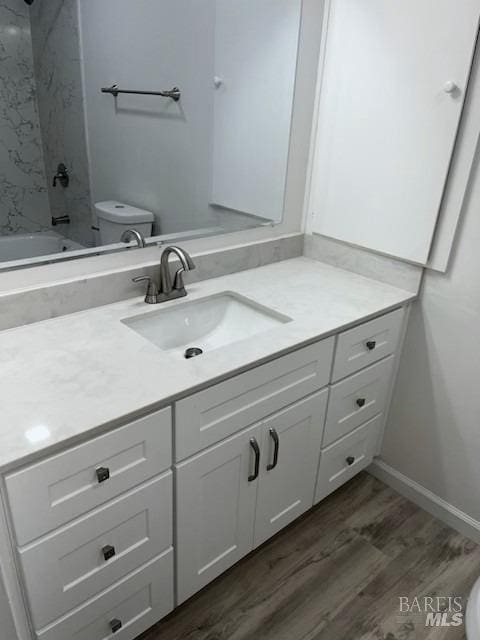 bathroom with toilet, wood finished floors, vanity, and  shower combination