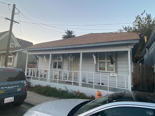 bungalow-style house with a shingled roof, covered porch, and fence