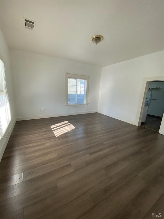 unfurnished room featuring baseboards, dark wood finished floors, and visible vents