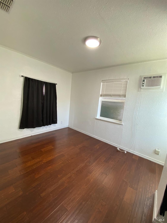 empty room with a wall mounted AC, visible vents, a textured ceiling, and wood finished floors