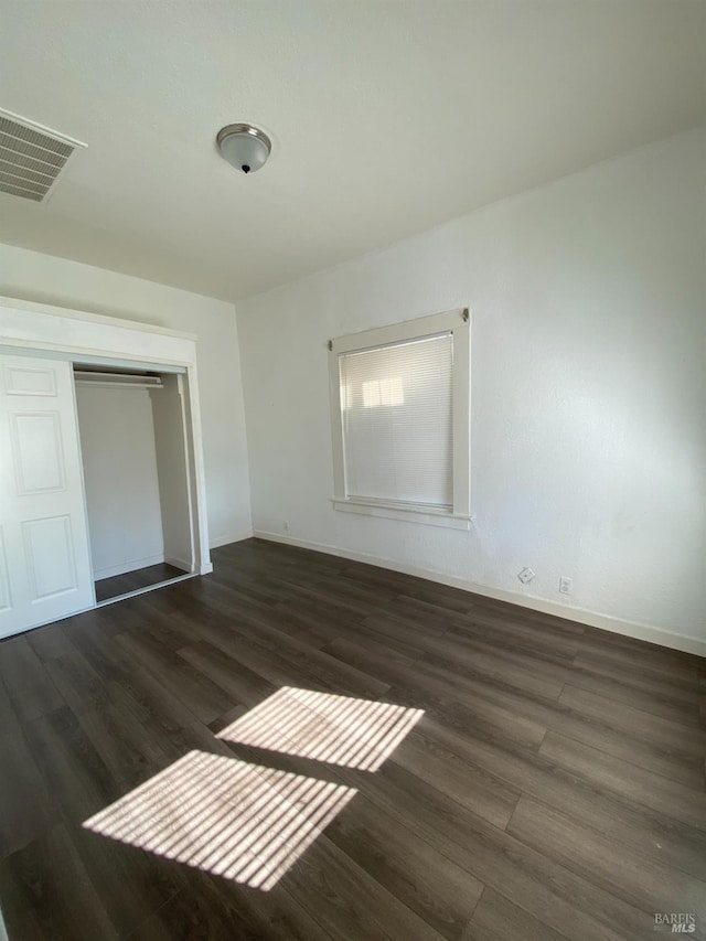 unfurnished bedroom featuring baseboards, wood finished floors, a closet, and visible vents