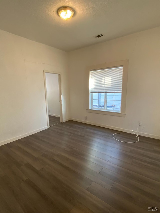 empty room featuring visible vents, a textured ceiling, baseboards, and dark wood-style floors