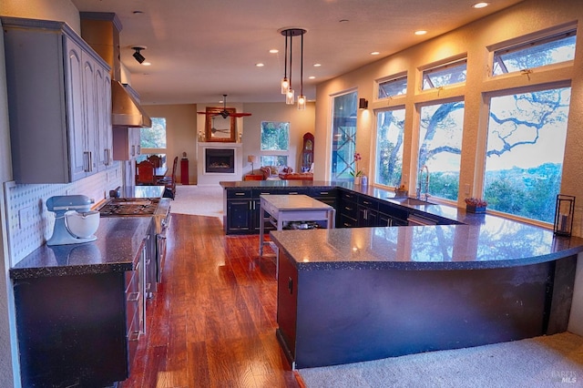 kitchen featuring stainless steel range, dark wood-type flooring, backsplash, decorative light fixtures, and a kitchen island