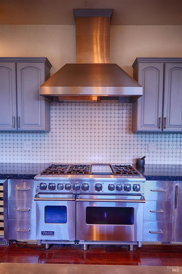 kitchen featuring backsplash, double oven range, dark stone countertops, and wall chimney range hood