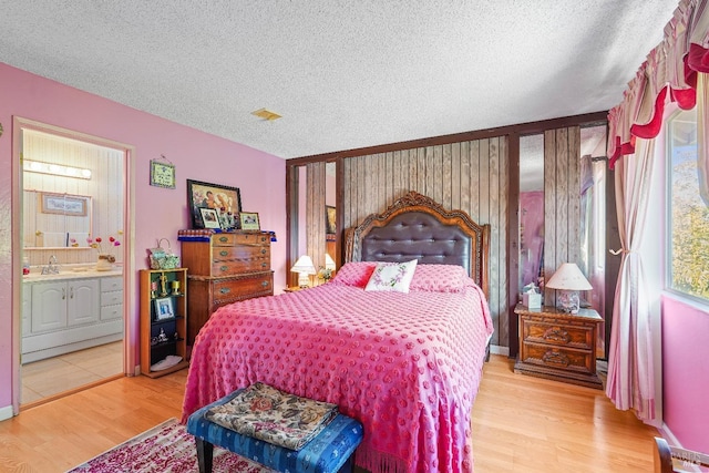 bedroom with ensuite bathroom, wood-type flooring, and a textured ceiling