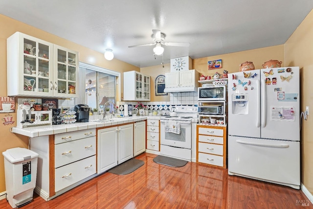 kitchen with light wood-type flooring, white appliances, sink, tile countertops, and white cabinetry