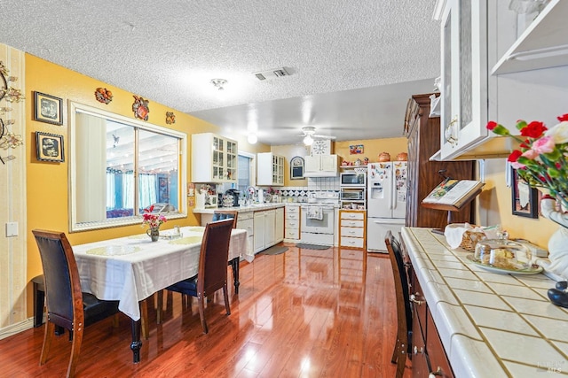 kitchen featuring white cabinetry, tile counters, wood-type flooring, a textured ceiling, and white appliances