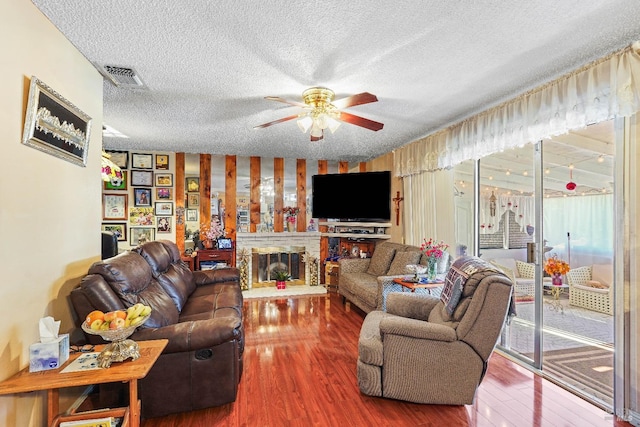 living room featuring ceiling fan, wood-type flooring, a textured ceiling, and a brick fireplace