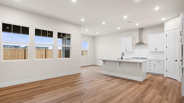 kitchen with white cabinetry, sink, wall chimney range hood, a center island with sink, and light hardwood / wood-style flooring