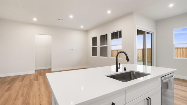 kitchen with dishwasher, an island with sink, sink, white cabinets, and light wood-type flooring