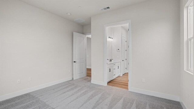 unfurnished bedroom featuring ensuite bathroom and light colored carpet