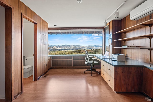 unfurnished office with a wall mounted AC, wooden walls, wood-type flooring, built in desk, and a mountain view