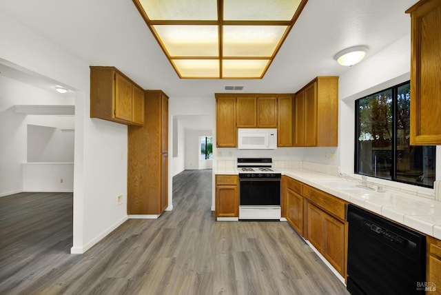 kitchen with tile countertops, light wood-type flooring, white appliances, and sink