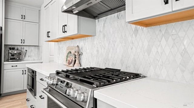 kitchen with stainless steel gas stove, backsplash, white cabinets, and wall chimney exhaust hood