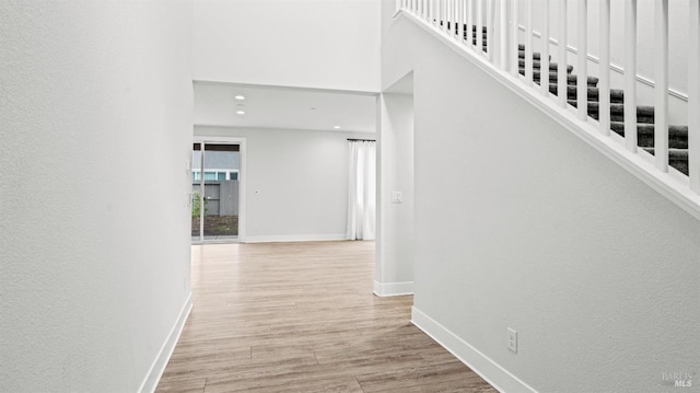 corridor featuring a towering ceiling and light hardwood / wood-style floors