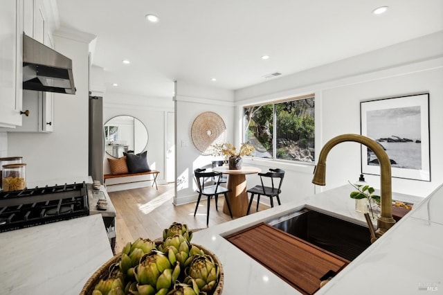 kitchen featuring ventilation hood, sink, light hardwood / wood-style flooring, light stone counters, and white cabinetry