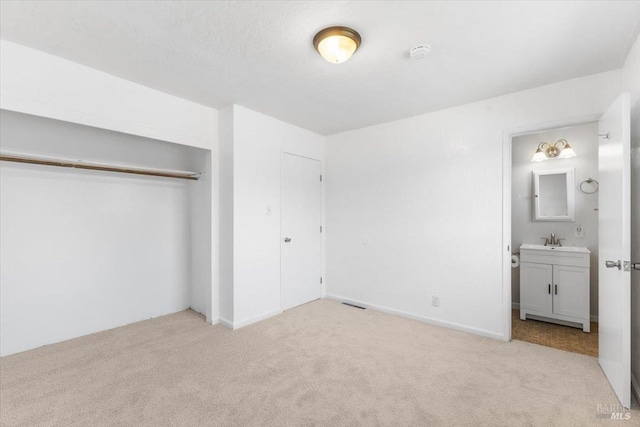 unfurnished bedroom with a closet, light colored carpet, connected bathroom, and a sink