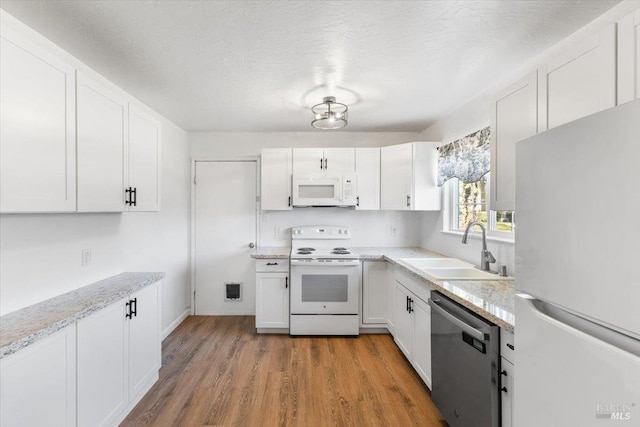 kitchen featuring white cabinets, white appliances, light wood-style floors, and a sink