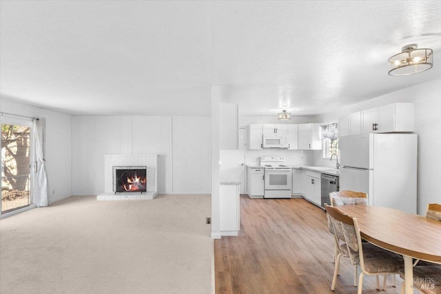 kitchen with a sink, white appliances, white cabinets, a fireplace, and light countertops