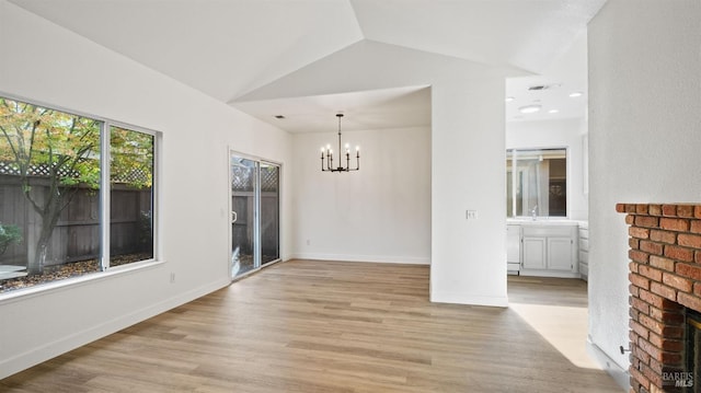 interior space featuring sink, an inviting chandelier, light hardwood / wood-style floors, vaulted ceiling, and a fireplace